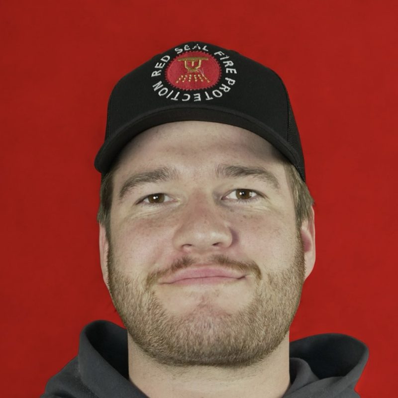 Levi Rock in a Red Seal Fire Protection cap, in front of a red backdrop.